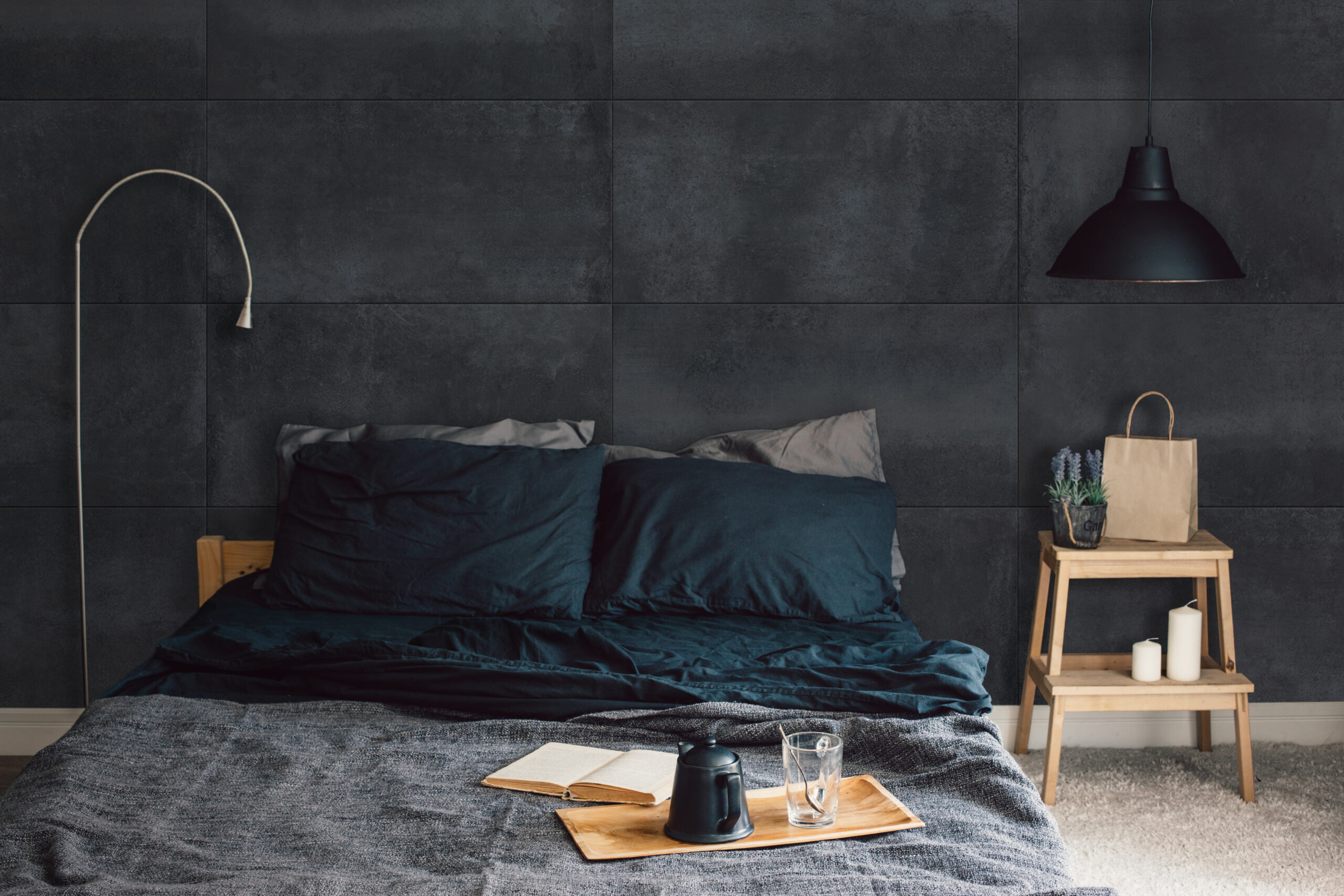 Black stylish loft bedroom. Unmade bed with breakfast and reading on tray. Lamp and interior decor over blank blackboard wall with copyspace. Cozy modern living space.